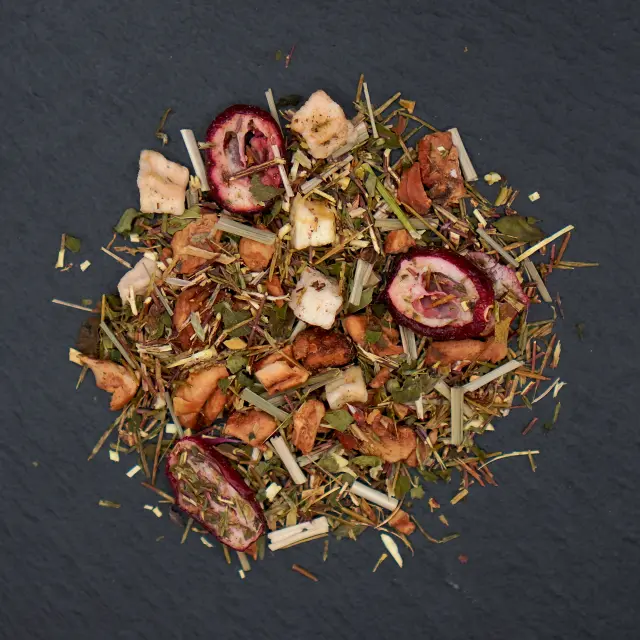 Un amestec de ceai de merișoare și mandarine, cu bucăți de fructe uscate, ierburi și frunze, pe o suprafață închisă.