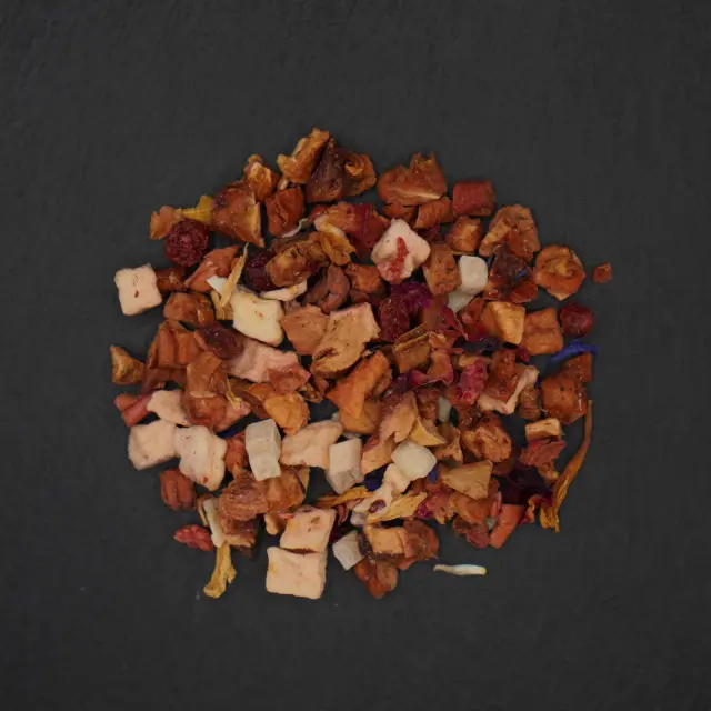 Un morman de bucăți de fructe uscate, inclusiv mere, ananas, căpșuni și flori, pe un fundal închis.