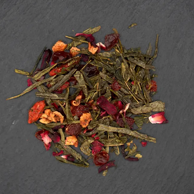 Un amestec de ceai Goji-Açai, cu frunze verzi de ceai, fructe de goji roșii și bucăți de fructe de açai, pe o suprafață închisă la culoare.